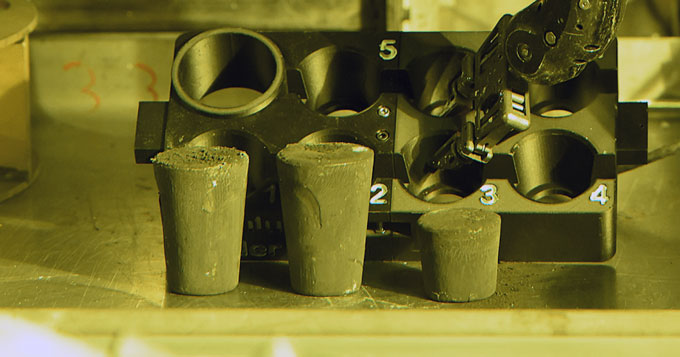 Three cylindrical pellets of HALEU fuel stand in front of laboratory equipment