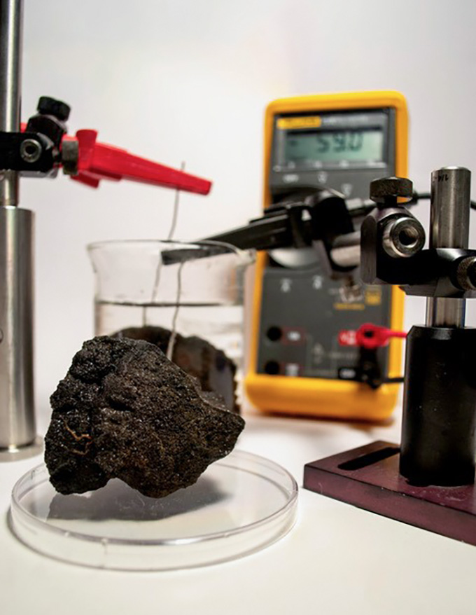 In a lab, wires held by clamps poke out of a metal-rich chunk retrieved from the seafloor in an experiment testing the nodule's electric potential.